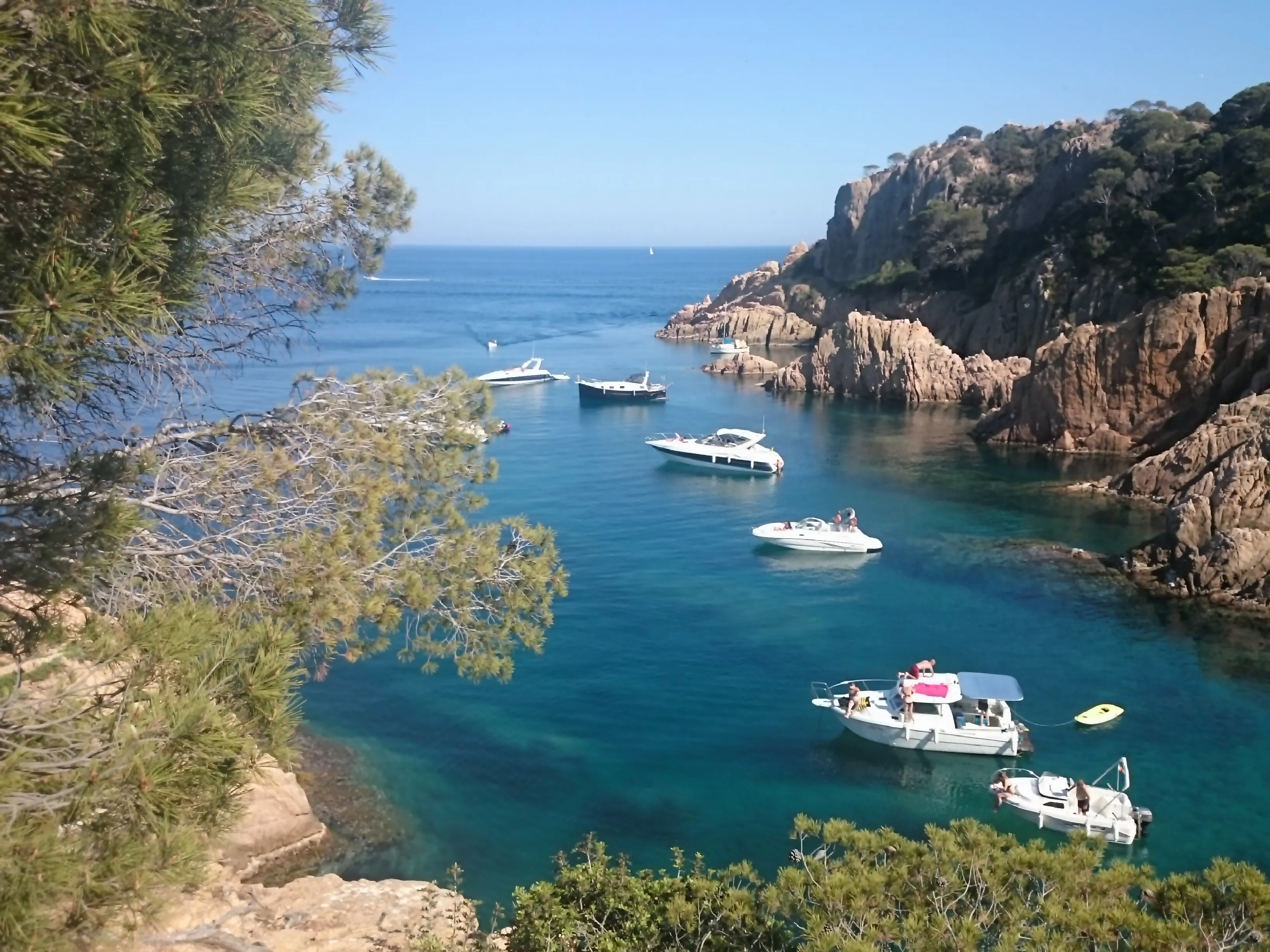 Boats anchored in a clear turquoise bay, surrounded by rocky cliffs and lush green trees